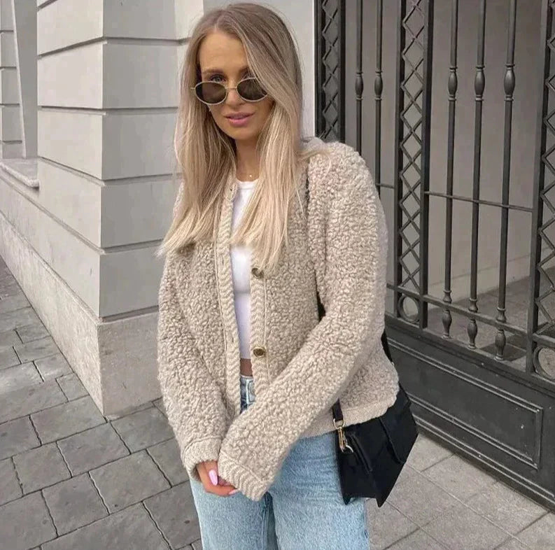 Frau trägt beigefarbenes Teddy Cardigan mit Knöpfen und schwarze Jeans